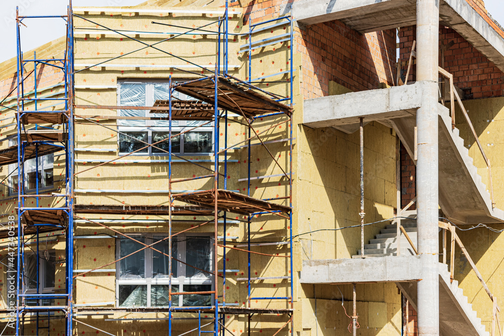 Thermal insulation of a red brick house with mineral wool. The use of scaffolding when building a house.