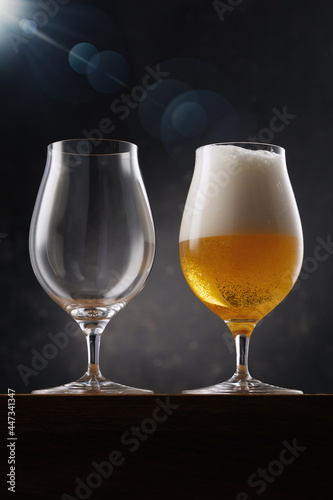 Two beer glasses. Glass full of light yellow beer and empty glass on a dark background. Selective focus