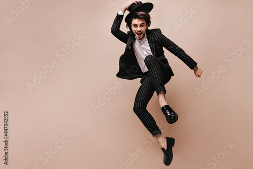 Attractive young brunette having fun and posing extraordinary against beige background. Man wearing white shirt, black striped suit, classic hat and elegant shoes photo