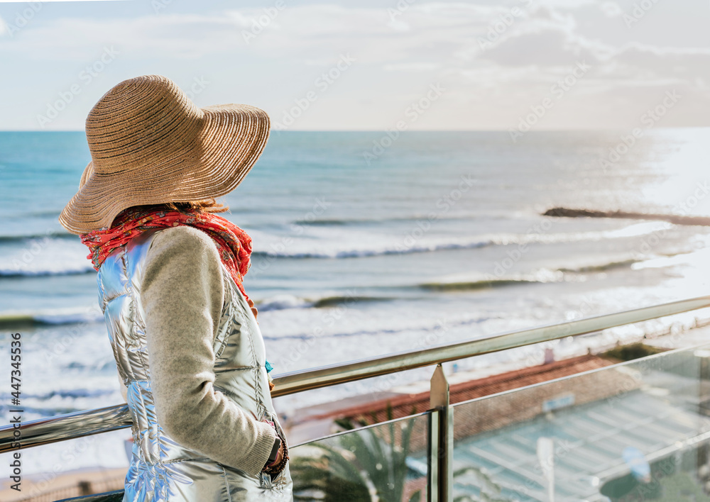 a woman in a hat contemplates the autumn sunset from a terrace on the coast.