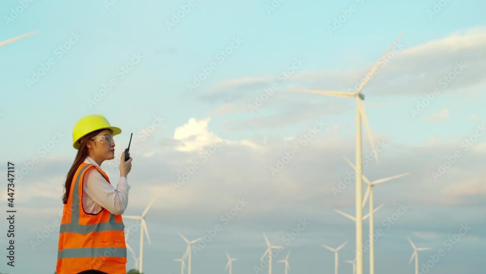 young female engineer using walkie talkie to checking system against wind turbine farm young female engineer using walkie talkie to checking system against wind turbine farm