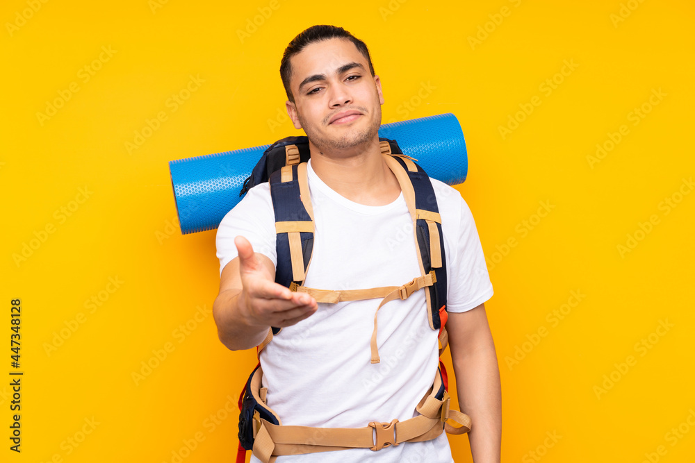 Young mountaineer asian man with a big backpack isolated on yellow background handshaking after good deal Young mountaineer asian man with a big backpack isolated on yellow background handshaking after good deal