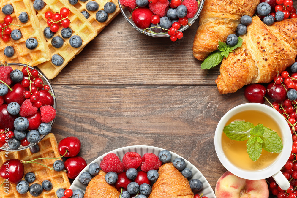 Frame with croissants, waffles, berries and fruits with cup of tea at the brown wooden background top view, copy space for text
