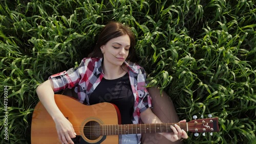 TOP view, Woman lies in a wheat field plays music on guitar and sings, in slow motion at sunset