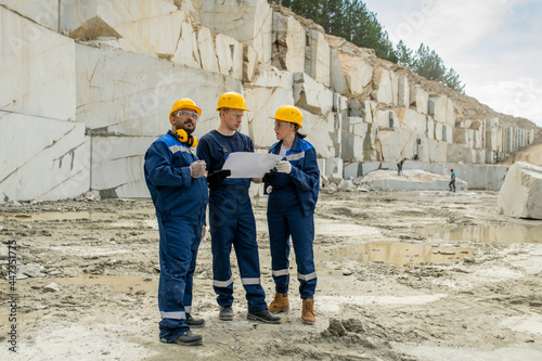 Team of contemporary miners in workwear discussing blueprint at quarry © pressmaster
