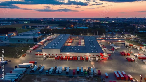 Hyper lapse (hyperlapse - motion time lapse) of a logistics park with a loading hub. Semi-trailer trucks standing at warehouse ramps for loading and unloading goods at dusk. Aerial panoramic view photo