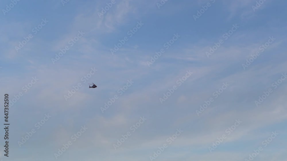 Tracking shot of helicopter flying in sunny day on background of blue cloudy sky. Remote view of helicopter hovering against bright sunny and cloudy sky, camera follows the helicopter. Tracking shot of helicopter flying in sunny day on background of blue cloudy sky. Remote view of helicopter hovering against bright sunny and cloudy sky, camera follows the helicopter.