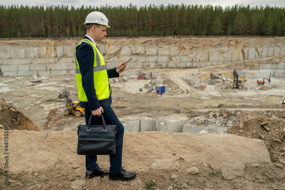 Young foreman with handbag and digital tablet walking along quarry Young foreman with handbag and digital tablet walking along quarry