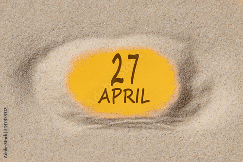 April 27. 27th day of the month, calendar date. Hole in sand. Yellow background is visible through hole. Spring month, day of the year concept photo