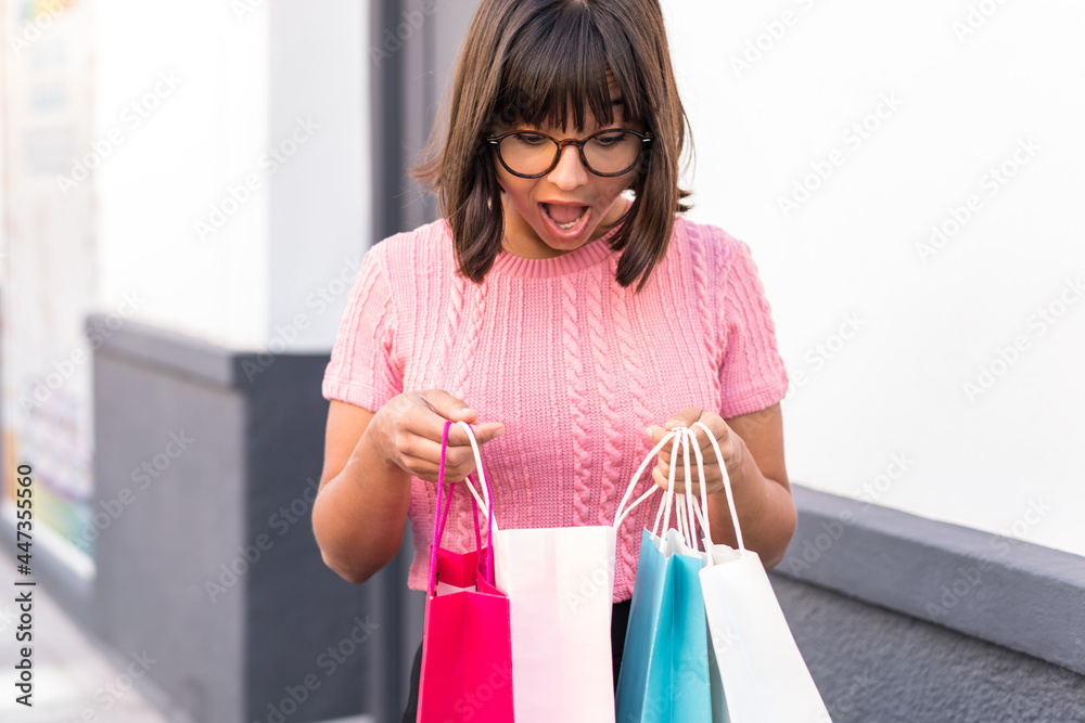 Young brunette woman in the city holding shopping bags and looking inside it Young brunette woman in the city holding shopping bags and looking inside it