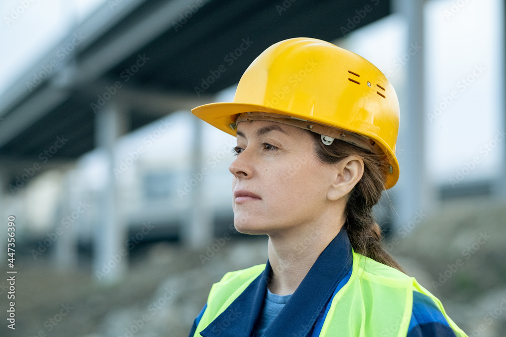 Close-up of young woman in work helmet looking away while standing on construction site outdoors Close-up of young woman in work helmet looking away while standing on construction site outdoors