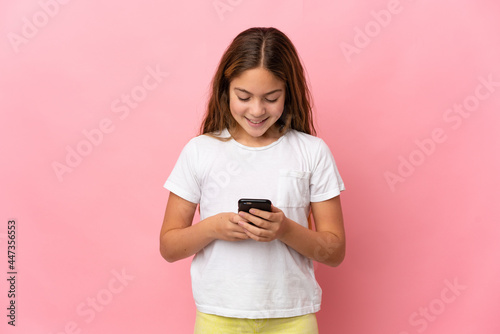 Child over isolated pink background sending a message or email with the mobile