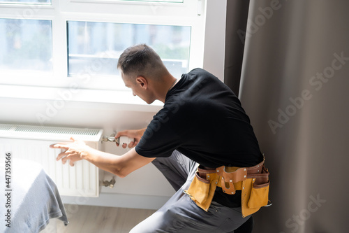 Slika na platnu young man plumber checking radiator while installing heating system in apartment