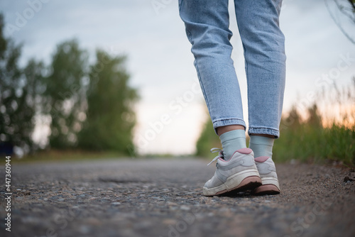 Woman legs in the shoes and jeans on the countryside road. Person waits the bus or a car.
