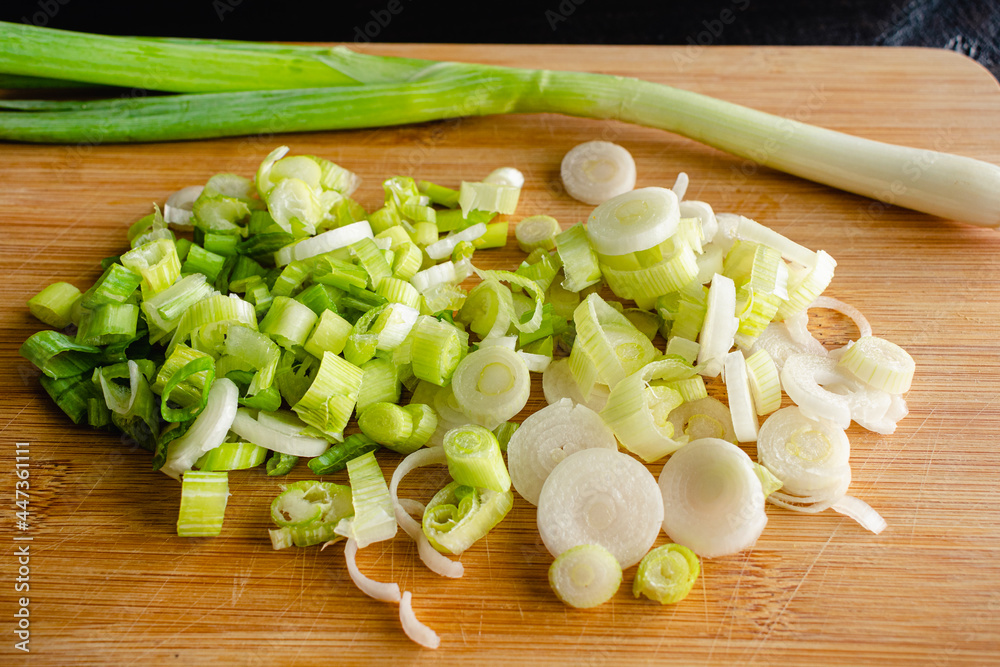 Closeup View of a Sliced Green Onion on a Bamboo Cutting Board: Slices of scallion on a wooden cutting board with a whole scallion in the background Closeup View of a Sliced Green Onion on a Bamboo Cutting Board: Slices of scallion on a wooden cutting board with a whole scallion in the background