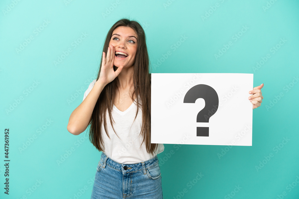 Young caucasian woman isolated on blue background holding a placard with question mark symbol and shouting Young caucasian woman isolated on blue background holding a placard with question mark symbol and shouting