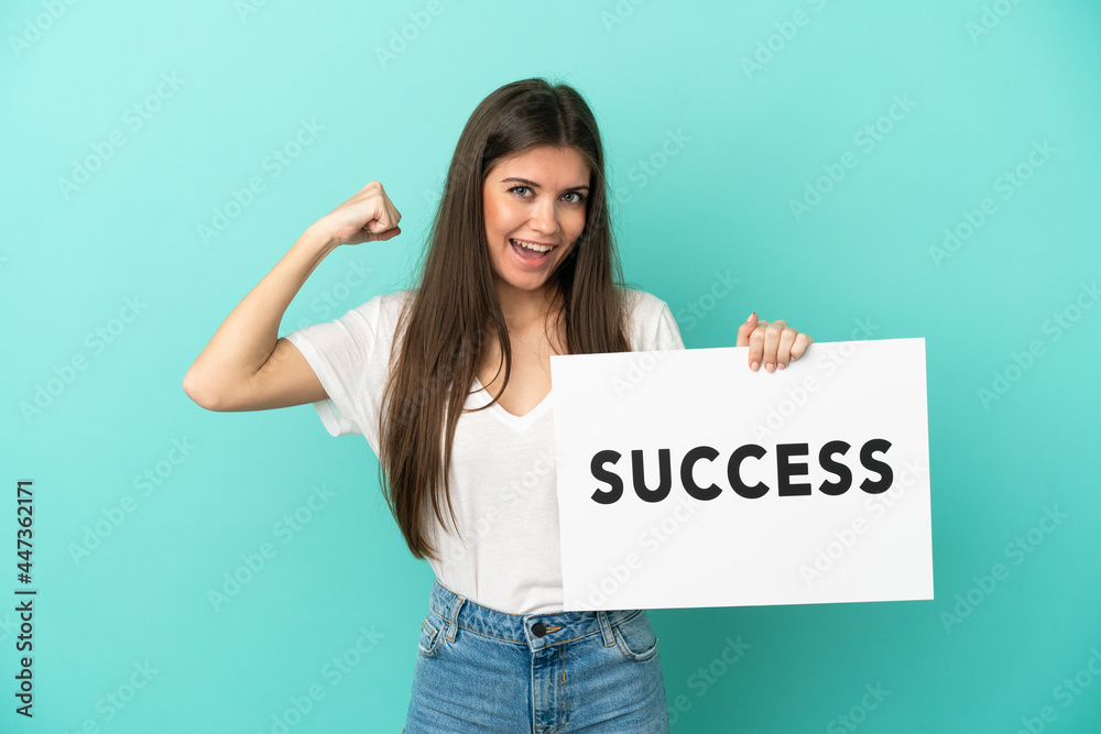 Young caucasian woman isolated on blue background holding a placard with text SUCCESS and doing strong gesture Young caucasian woman isolated on blue background holding a placard with text SUCCESS and doing strong gesture
