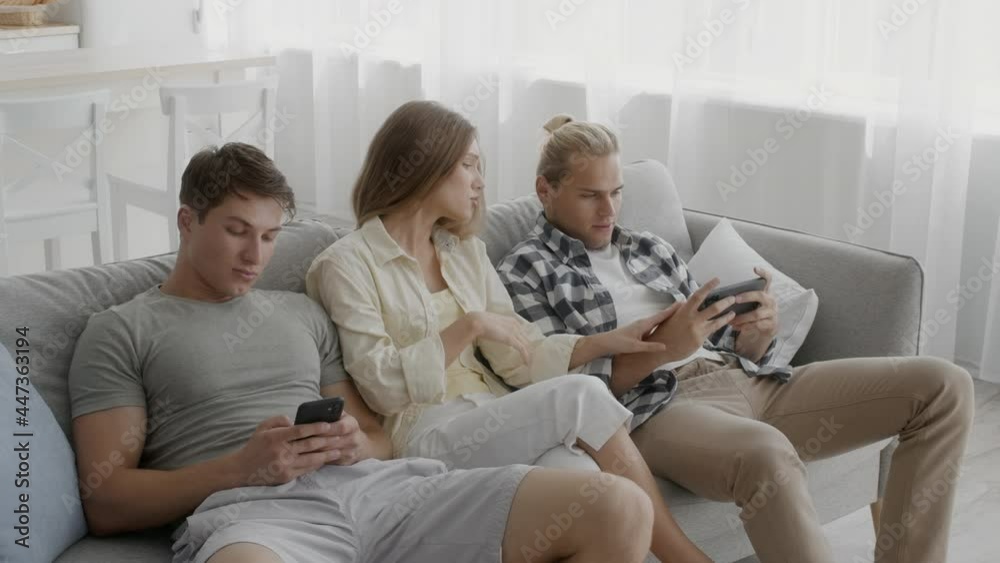 Bored young woman sitting on couch between gadget addicted friends with smartphones Bored young woman sitting on couch between gadget addicted friends with smartphones