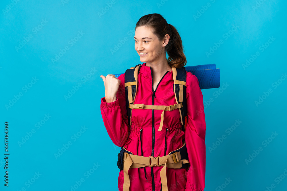 Young mountaineer woman over isolated blue background pointing to the side to present a product Young mountaineer woman over isolated blue background pointing to the side to present a product