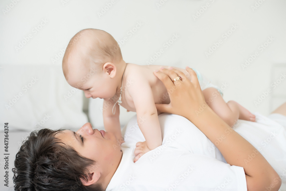Mother and child on a white bed. Mom and baby boy in diaper playing in bedroom. Parent and little kid relaxing at home. Family having fun together. Mother and child on a white bed. Mom and baby boy in diaper playing in bedroom. Parent and little kid relaxing at home. Family having fun together.