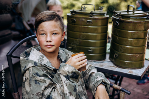 Boy in camouflage relax and drinks tea after playing in laser tag shooting game with a weapon outdoor