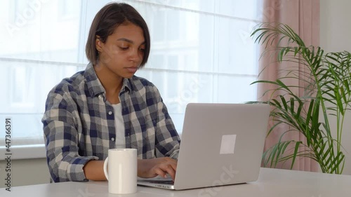 Young woman sitting at a computer desk using a laptop working online at home. Cozy office workplace, remote work, e-learning concept