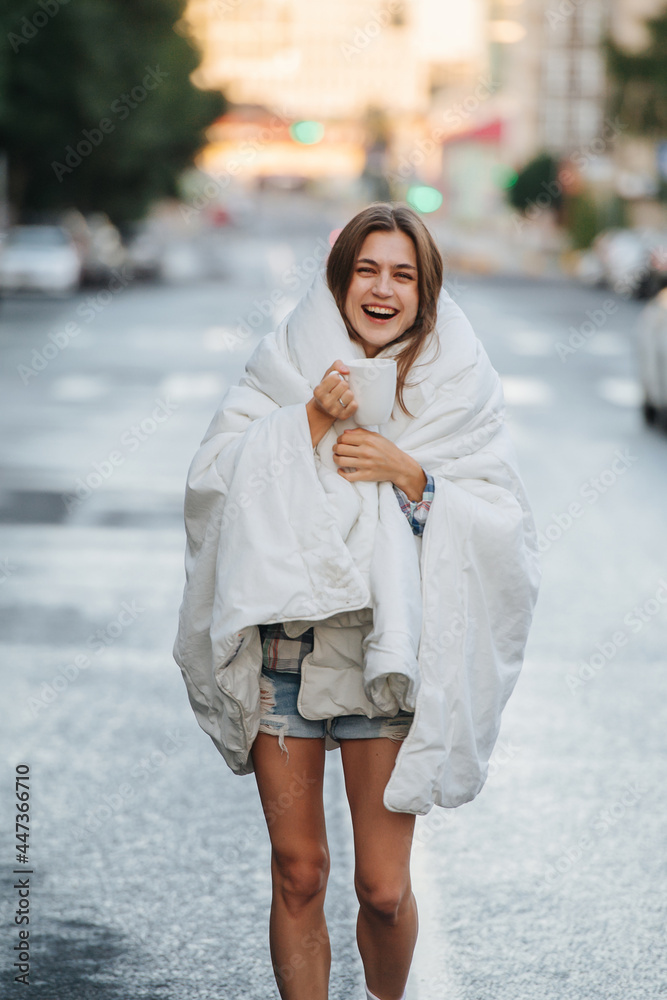 Unruly woman wrapped in blanket drinking coffee in the middle of empty city road Unruly woman wrapped in blanket drinking coffee in the middle of empty city road