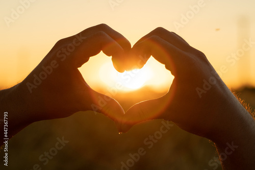 The silhouette of a hand in the shape of a love heart at sunset. Hands forming a heart shape with sunset silhouette