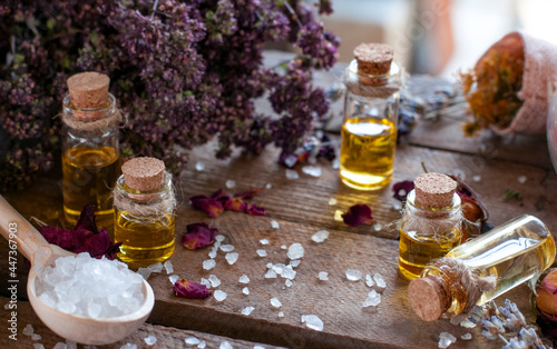 essential oil bottles with dry ingredients of rose, lavender  and white crystals in the spoon on the wood table	
