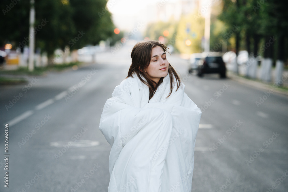 Blissful cozy woman wrapped in blanket in an empty city road in the morning