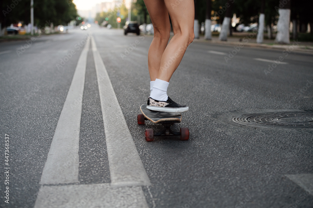 Legs of a woman riding on a skateboard on an empty city road