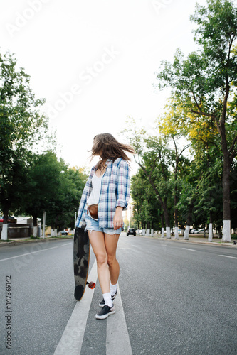 Rebellous woman walking in the middle of an empty city road with skateboard in hand