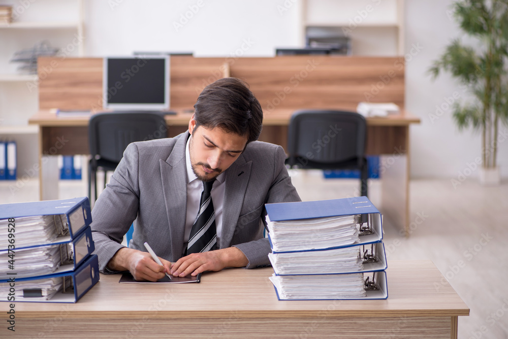 Young male employee unhappy with excessive work in the office Young male employee unhappy with excessive work in the office