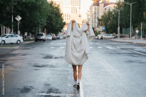 Bare legged woman wrapped in blanket walking down empty city road in the morning © zzzdim