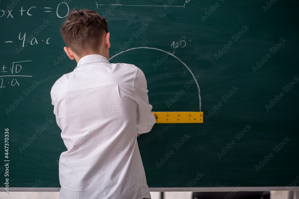 Schoolboy studying geometry in front of blackboard