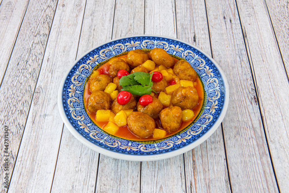 Lifetime popular Chinese restaurant recipe. Stew of breaded pork balls with sweet and sour sauce and pieces of peach and cherries on a blue plate Lifetime popular Chinese restaurant recipe. Stew of breaded pork balls with sweet and sour sauce and pieces of peach and cherries on a blue plate