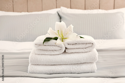 Fototapeta Naklejka Na Ścianę i Meble -  Stack of fresh towels with flower on bed indoors