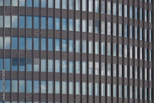 Typical modern facade with rectangular grid frame structure and reflection of blue sky on reflective glass of high rise office building. 