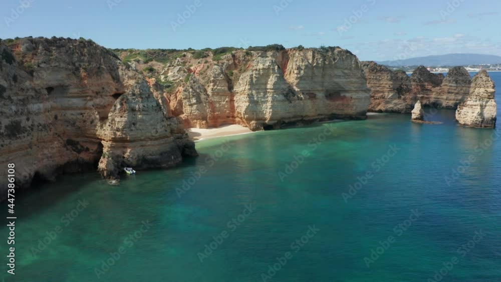 Cinematic aerial reveal of a small anchored boat near rocky cliffs and a small sand beach Cinematic aerial reveal of a small anchored boat near rocky cliffs and a small sand beach