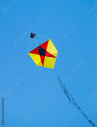 pipa brasileira amarela e vermelha com desenho geométrico voando em ceu azul