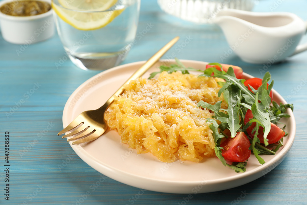 Tasty spaghetti squash with tomatoes, cheese and arugula served on light blue wooden table Tasty spaghetti squash with tomatoes, cheese and arugula served on light blue wooden table