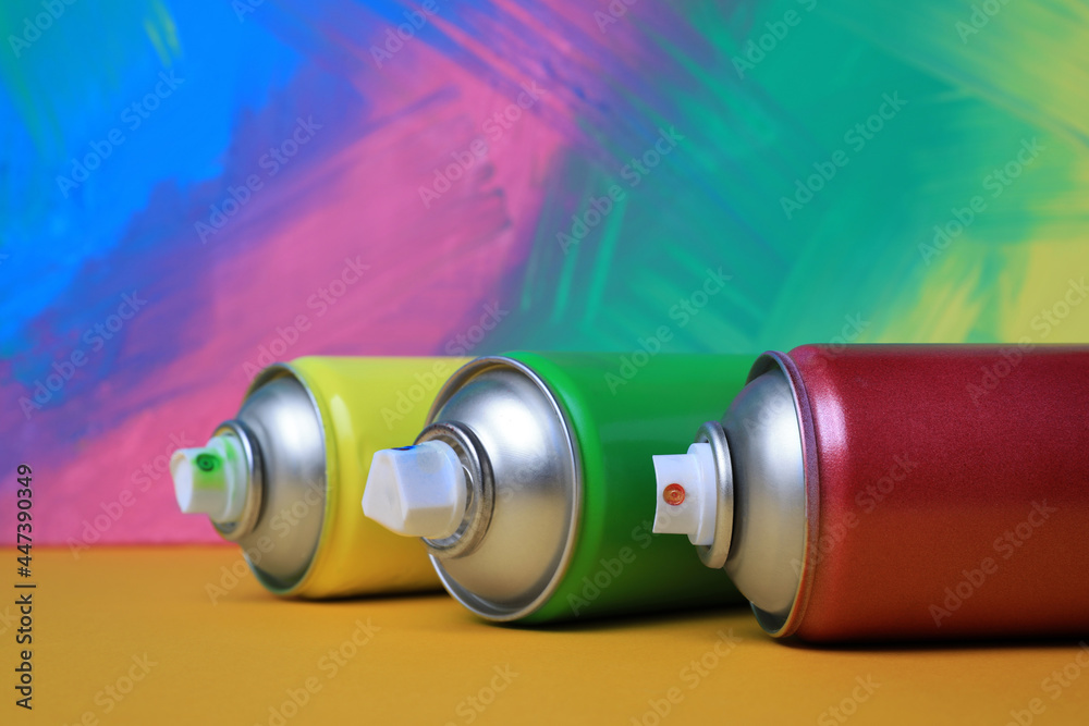 Cans of different spray paints on color background, closeup. Graffiti supplies