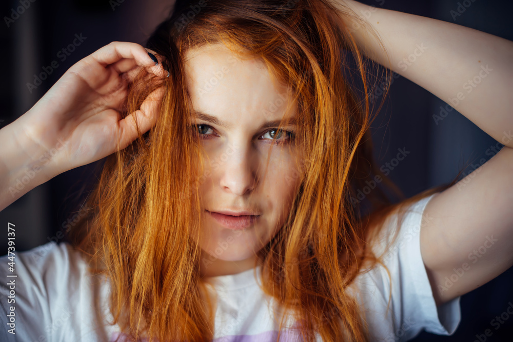 Fototapeta premium Portrait of beautiful adult young woman with red tousled hair, close-up, blurred background. Sexy brunette touches her long hair and looks at camera.