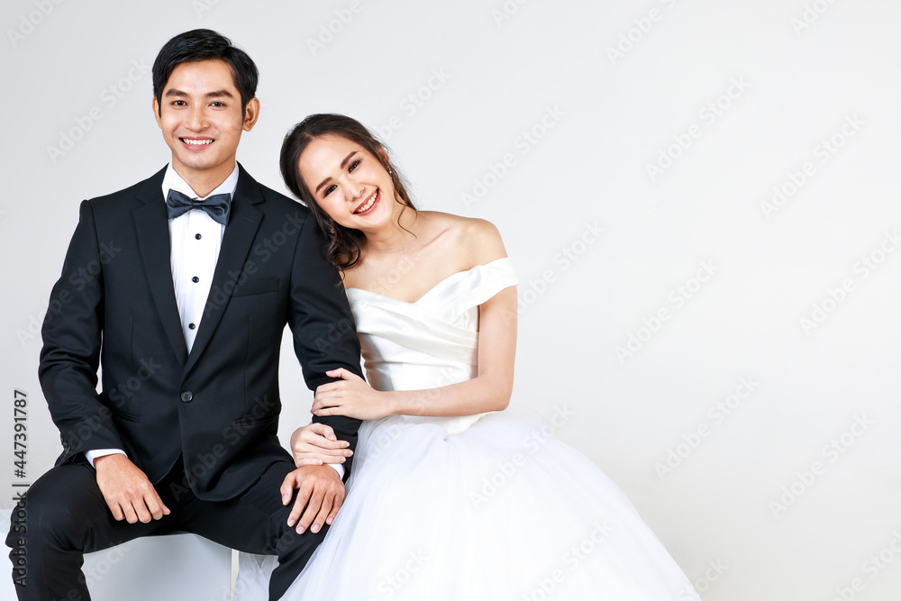 Young attractive Asian couple, soon to be bride and groom, woman wearing white wedding gown. Man wearing black tuxedo, sitting down together. Concept for pre wedding photography Young attractive Asian couple, soon to be bride and groom, woman wearing white wedding gown. Man wearing black tuxedo, sitting down together. Concept for pre wedding photography