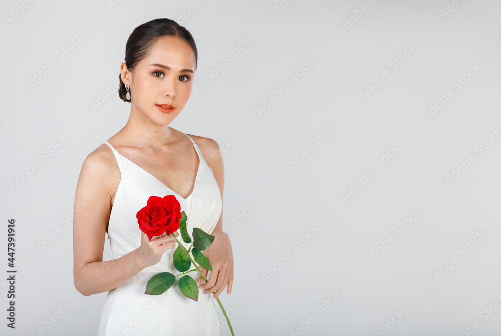 Portrait of young attractive Asian woman wearing white wedding dress holding red rose against white background. Concept for pre wedding photography Portrait of young attractive Asian woman wearing white wedding dress holding red rose against white background. Concept for pre wedding photography