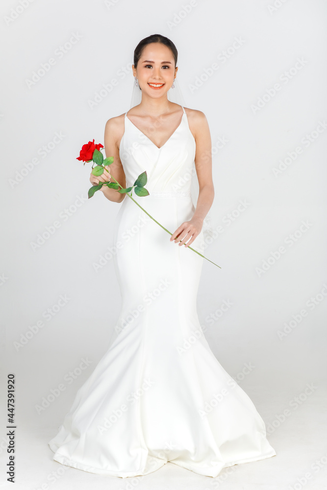 Full length of young attractive Asian woman wearing white wedding gown holding red rose against white background. Concept for pre wedding photography Full length of young attractive Asian woman wearing white wedding gown holding red rose against white background. Concept for pre wedding photography