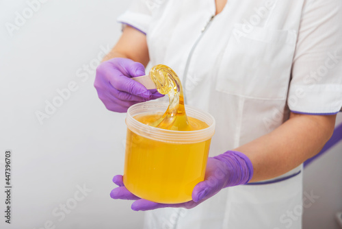 Natural honey sugar paste shugaring closeup. Women beautician holds jar wax of paste for sugar depilation shugaring, white background © kuzenkova