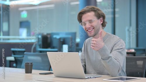 Thumbs Up by Young Man with Laptop at Work