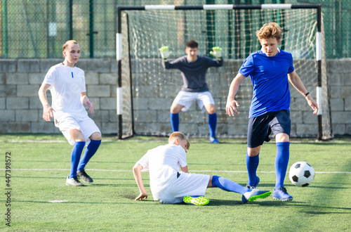 Game moments of football match between two teams of teenagers in white and blue shirts