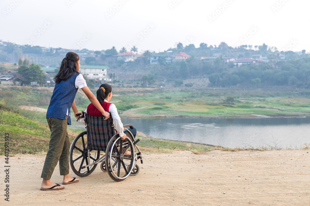 Disabled handicapped woman in wheelchair and care helper walking in park.